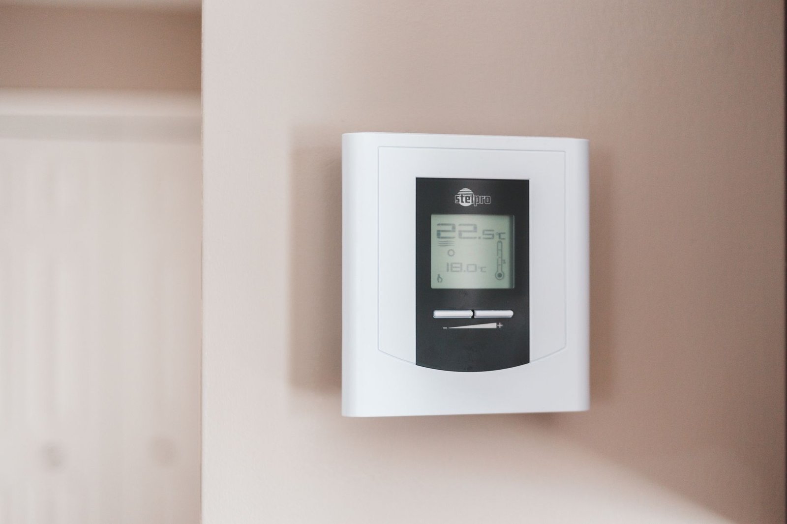 A modern programmable thermostat installed near a window air conditioning unit in a home.